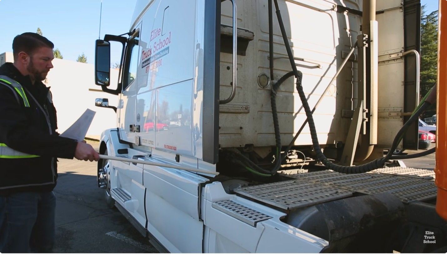 CDL student inspecting fuel tank area on an Elite Truck School semi-truck during a pre-trip inspection
