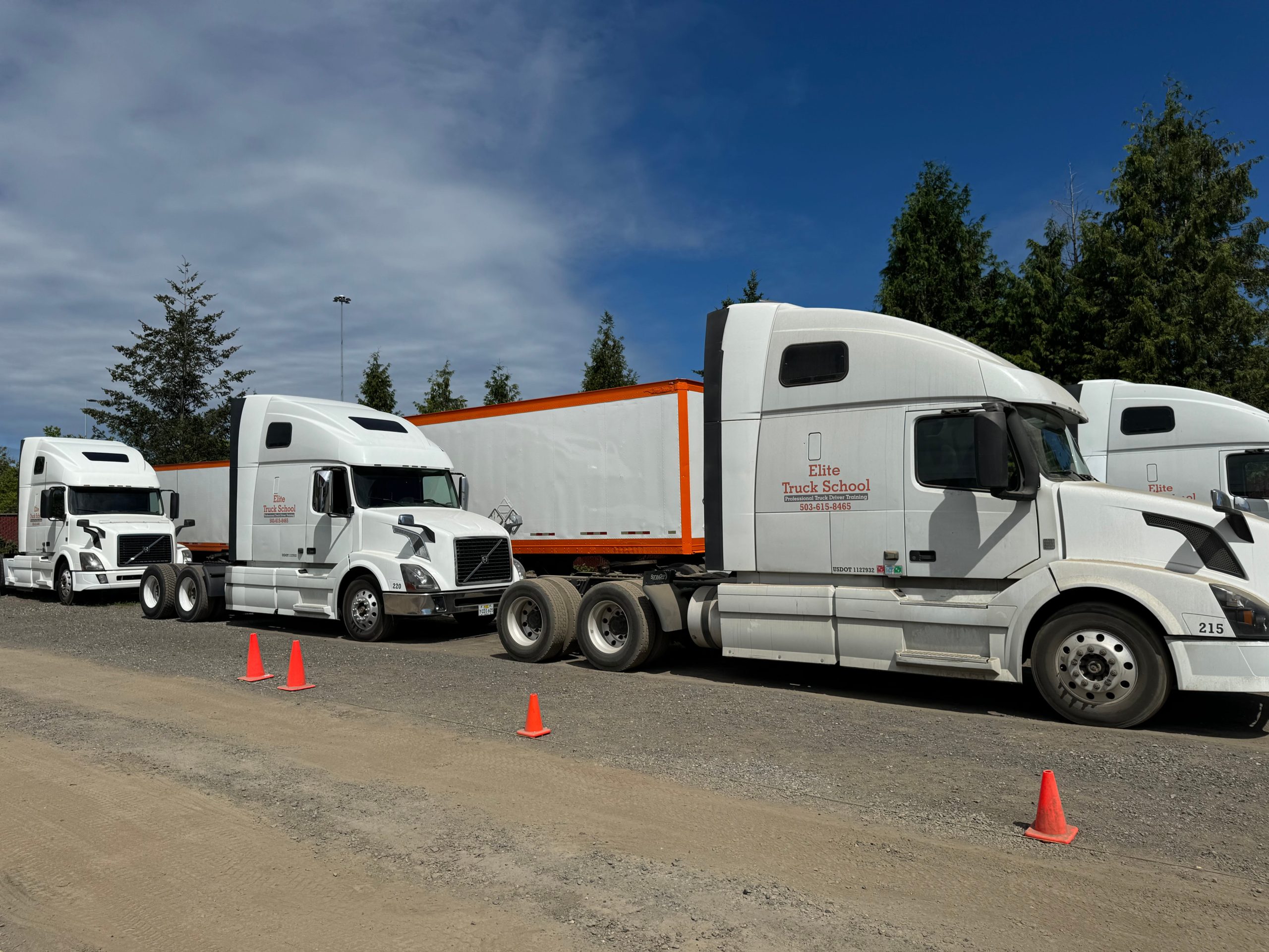 Four semi trucks parked in yard, shown from side angle