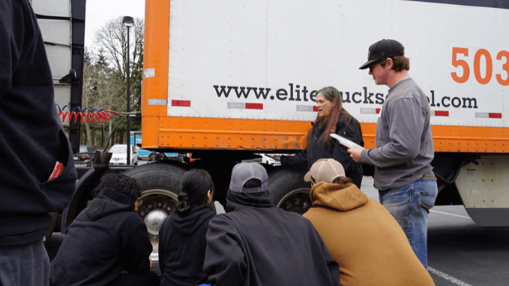 Nicole standing by semi truck trailer, students huddled around