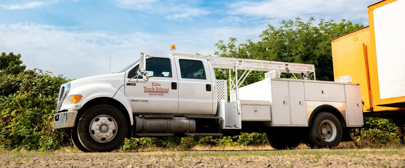 White Elite Truck School utility truck with a service bed parked outdoors beside greenery, used for Class B CDL training.