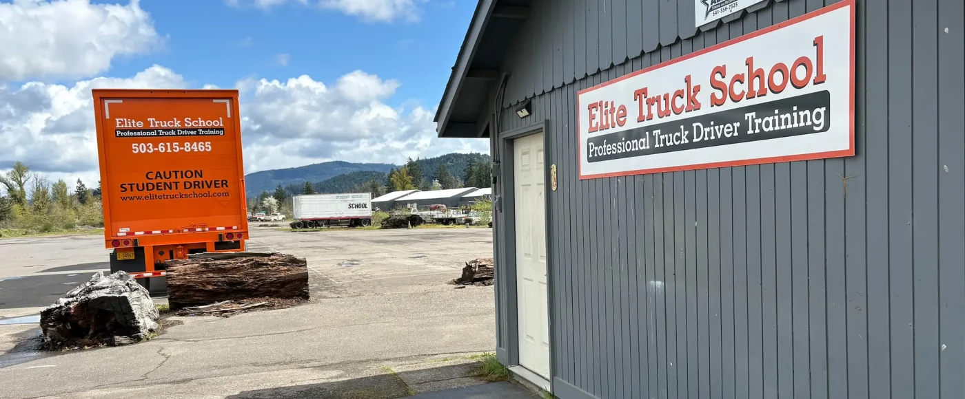 Exterior of the Eugene location, with a signed gray building, a trailer, and a training lot with trucks and mountains in the background.