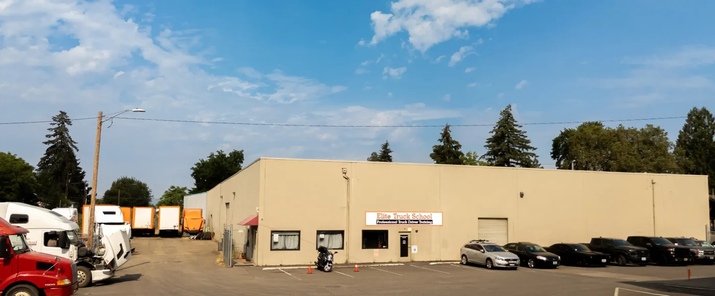 Exterior of the Hillsboro location, a tan building with a signed entrance, semi-trucks and trailers parked to one side, and cars in the lot.