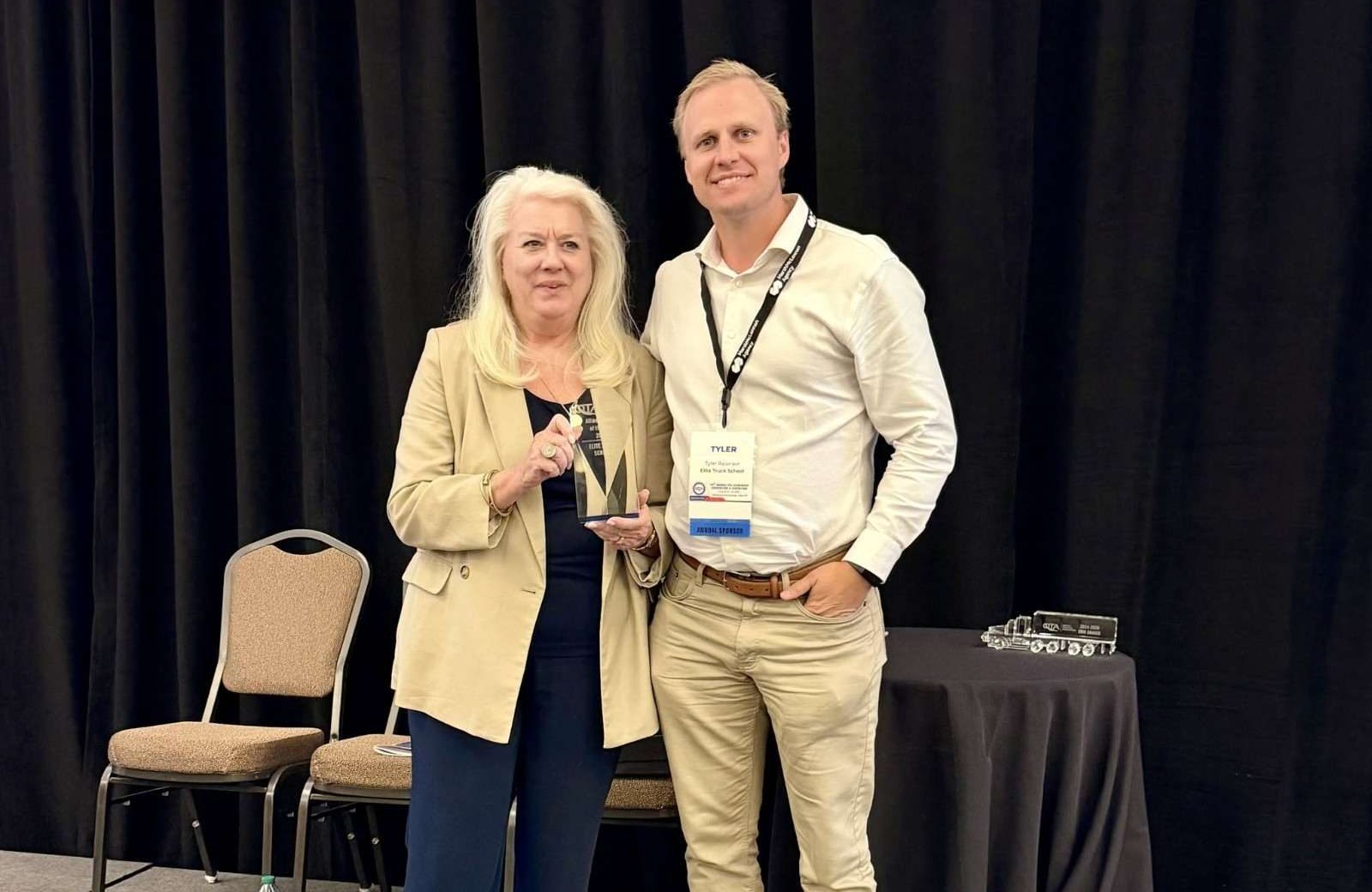 Tyler holding award plaque next to woman at conference