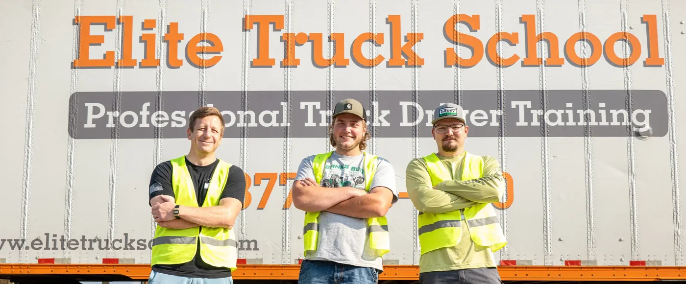Three Elite students standing with their arms cross in front of a trailer