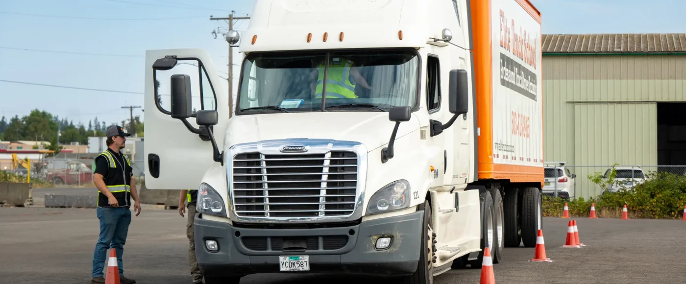 CDL instructors in safety vests guiding a student driving an Elite Truck School semi-truck through a cone course on a training lot.